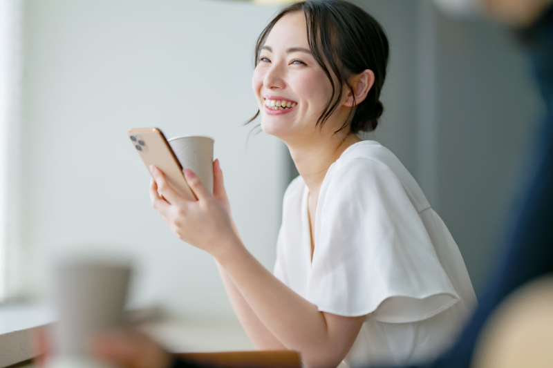 カフェでスマホを片手に寛ぐ笑顔の女性